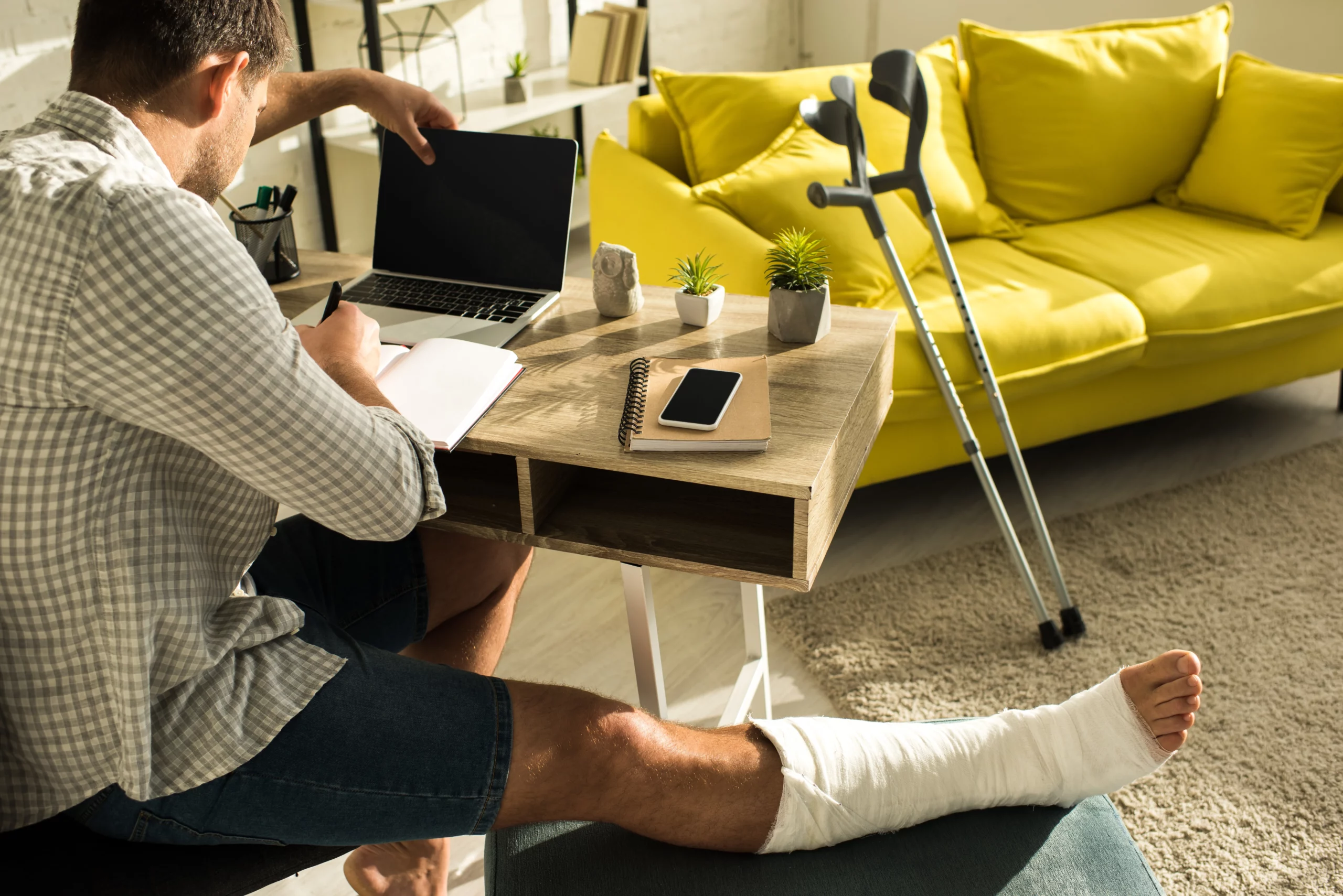 Back view of a person with a broken leg working on a laptop at home, illustrating personal injury recovery and the importance of meeting Texas personal injury filing deadlines for legal claims.